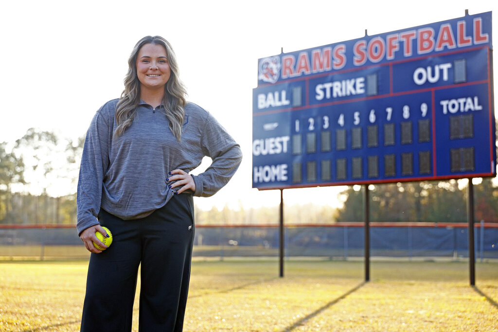 Head softball coach Morgan Britt stands next to the scoreboard.