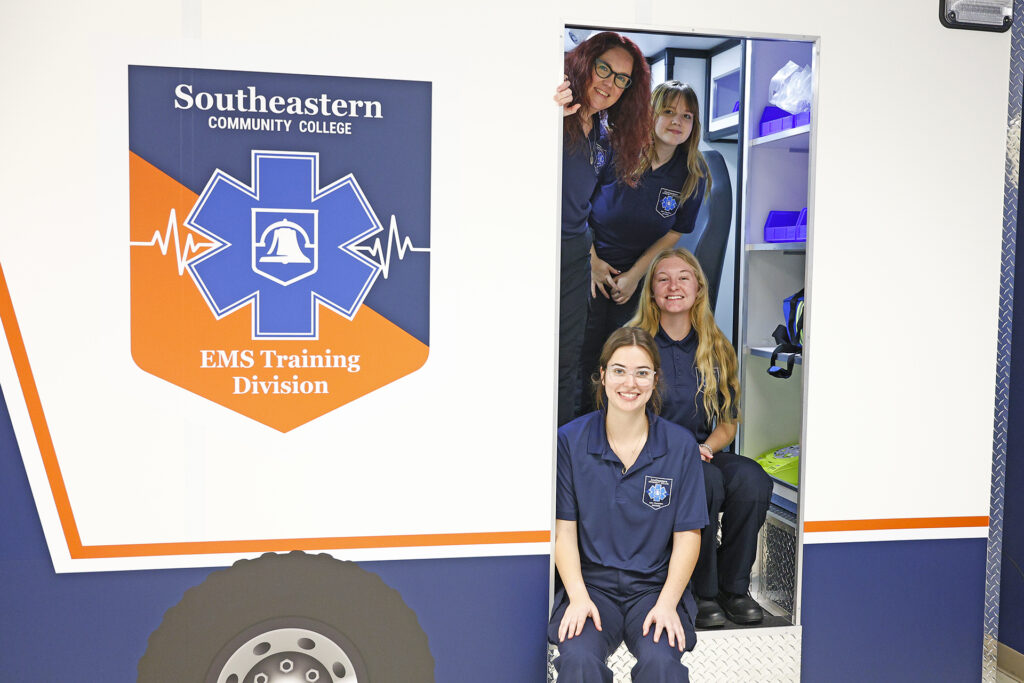EMS students pose at the side entrance of the ambulance simulator.