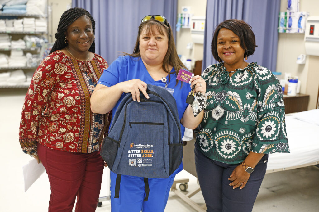 NCReconnect Student holding a Better Skills Better Jobs backpack and Walmart Gift Card with 2 SCC Employees