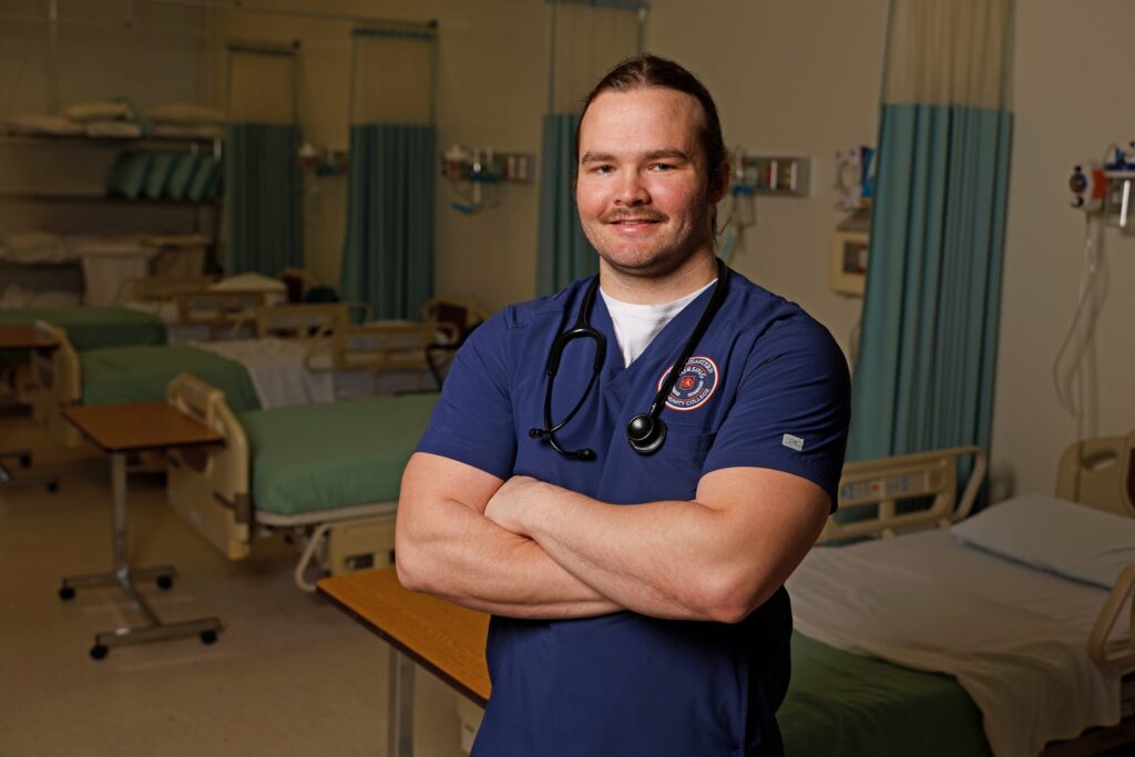 Aiken Ezzell standing in the Nursing Building in his SCC Blue Scrubs.