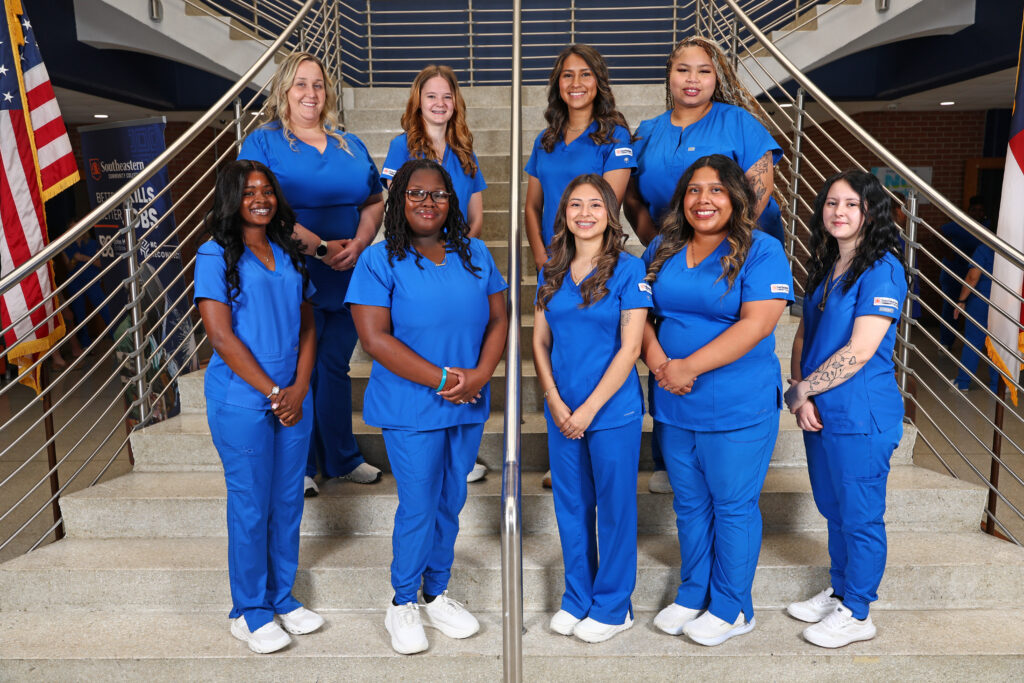 Phlebotomy graduates stand on the stairs in A-Building.