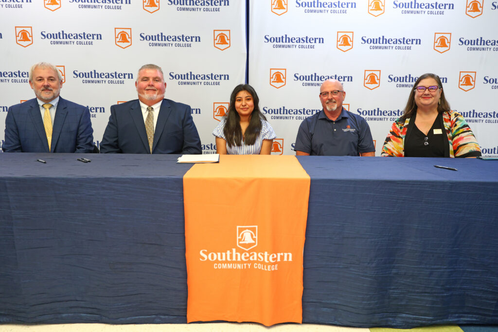 Viridiana Ramos (center) sits with Columbus County Schools, Southeastern Community College, and UNC Pembroke leadership at her scholarship signing ceremony.