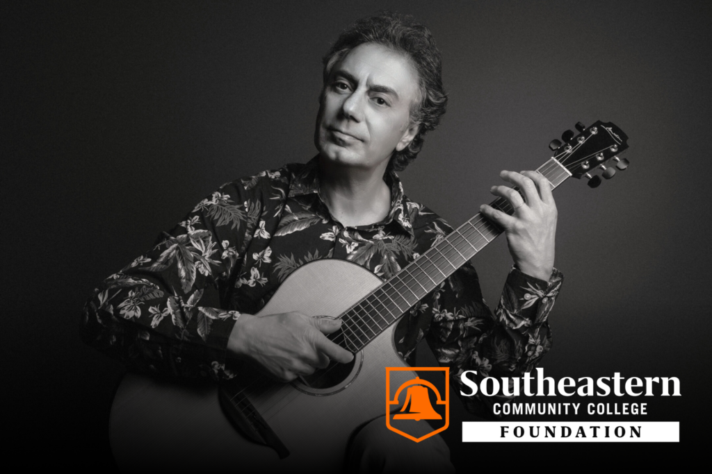 Pierre Bensusan playing guitar with the SCC Foundation logo in front