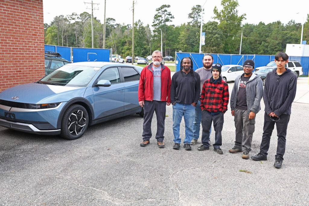 Johnny O'Connell stands with his automotive class next to the donated electric vehicle.